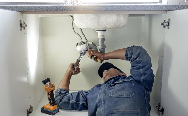Plumber repairing pipes beneath a bathroom sink in San Lorenzo
